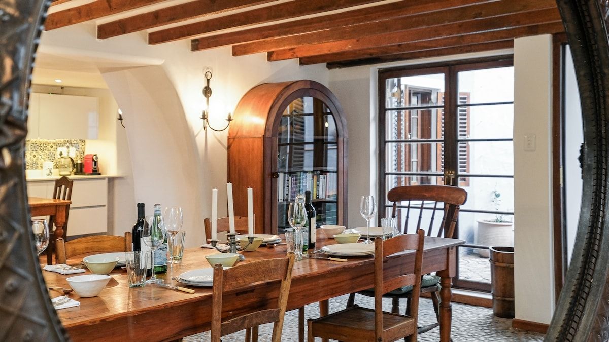 Un coin repas avec une table en bois dressée pour quatre personnes, une bibliothèque et une vue sur l’extérieur.