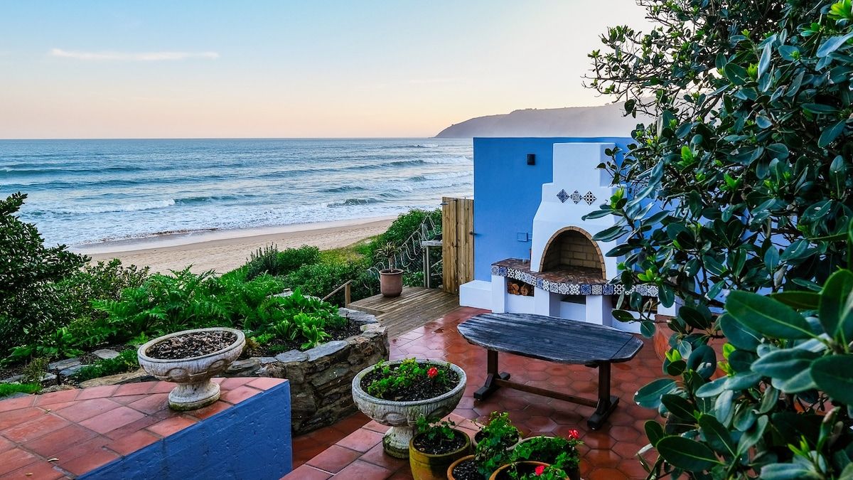 A patio with a view of the ocean, a barbecue area, and potted plants.