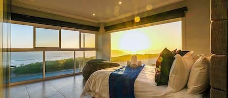 A bedroom with a large bed, a view of the ocean, and a sunset.