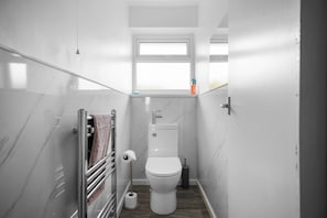 Ein kleines Badezimmer mit Toilette, Handtuchhalter, Fenster und Toilettenpapierhalter.