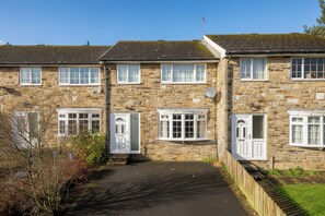 A stone-built residential building with multiple windows and doors, a paved driveway, and a wooden fence. - Whole House In The Yorkshire Dales Near Harrogate (Dacre Banks)