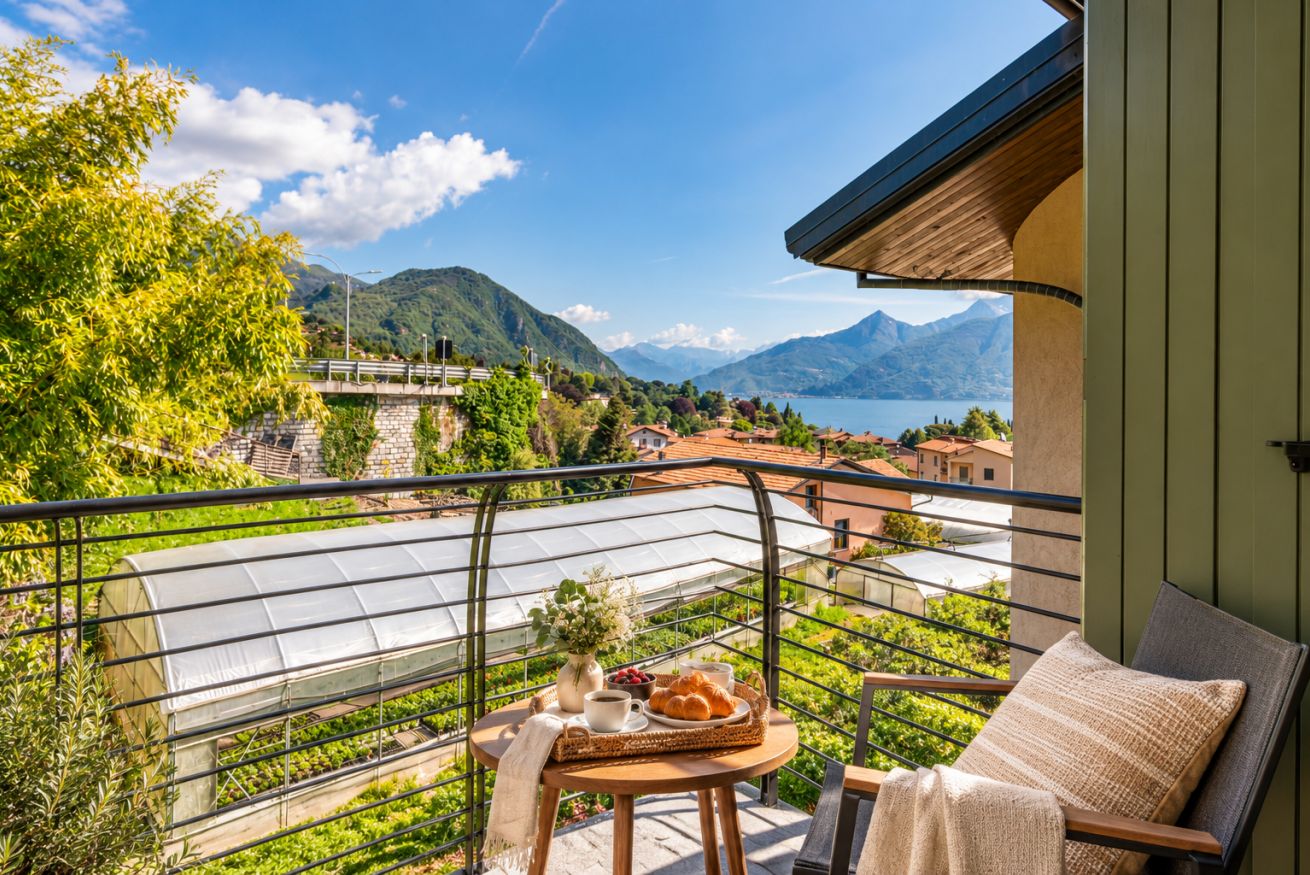 Un balcone con un tavolo apparecchiato per la colazione, con vista su un paesaggio montuoso e un lago.