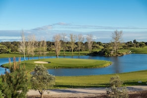 Un campo de golf con un lago, árboles y cielo despejado.