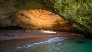 Una cueva con una gran formación rocosa y una zona de playa con gente y barcos.