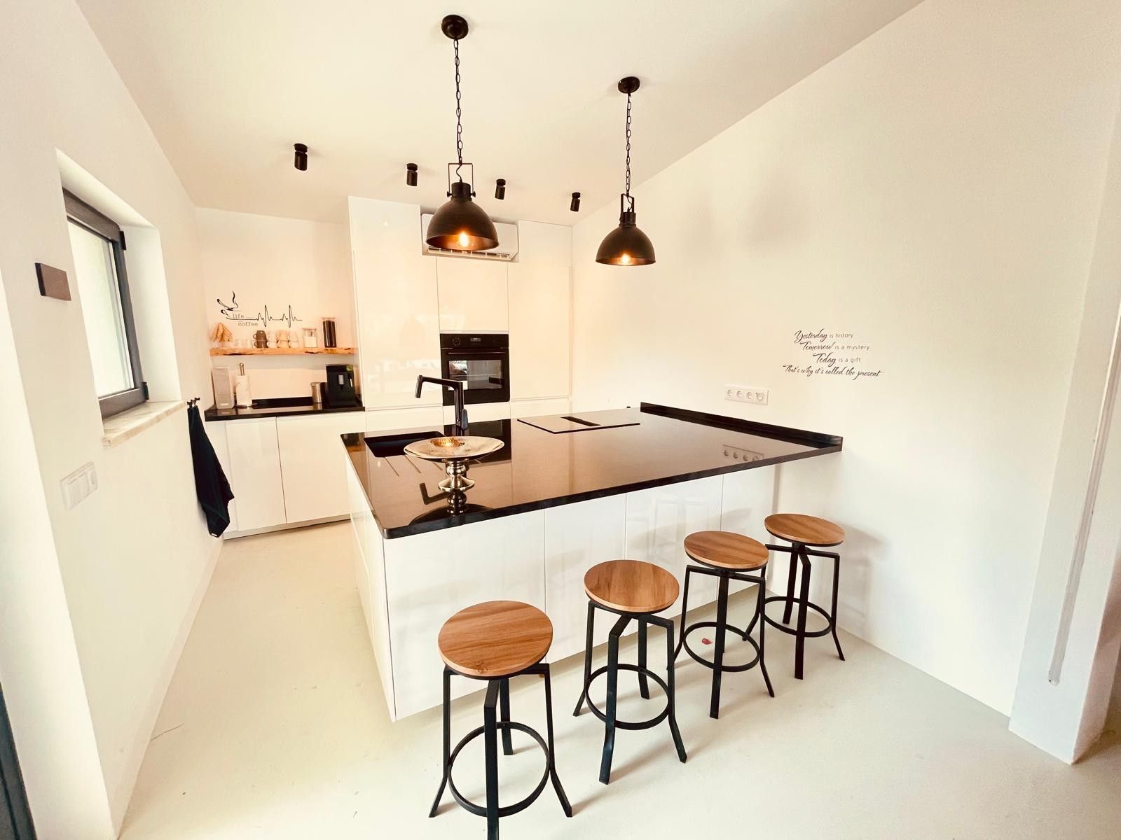 Une cuisine moderne dotée d’un îlot central, de tabourets de bar, de luminaires suspendus et d’un four fixé au mur.