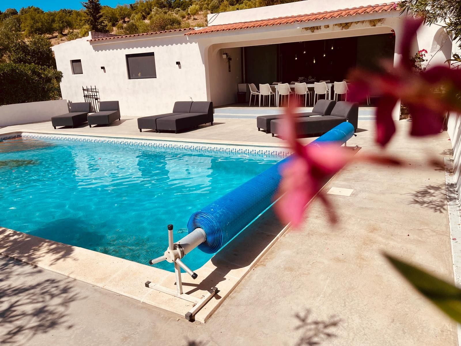 Una piscina con cubierta, mobiliario exterior y un edificio con techo de tejas.