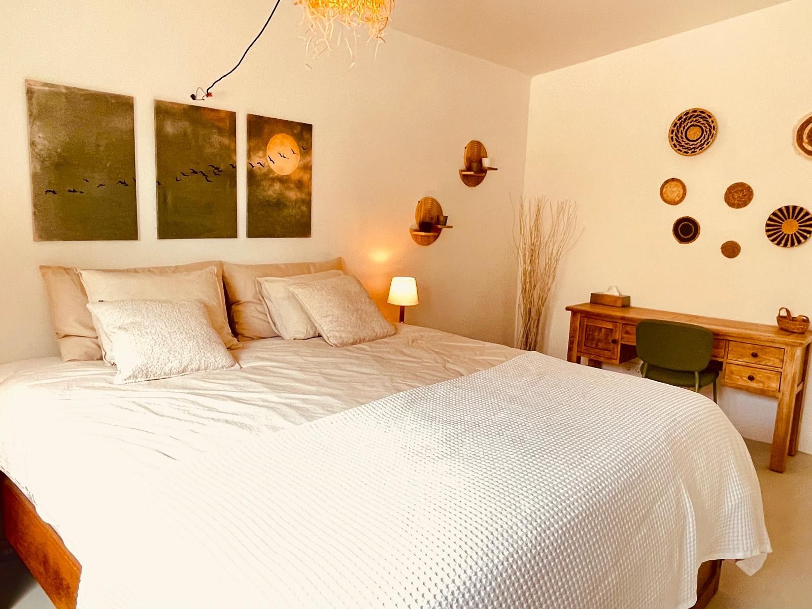 Un dormitorio con una cama grande, un escritorio y decoración en las paredes, incluyendo cuadros y elementos colgantes.