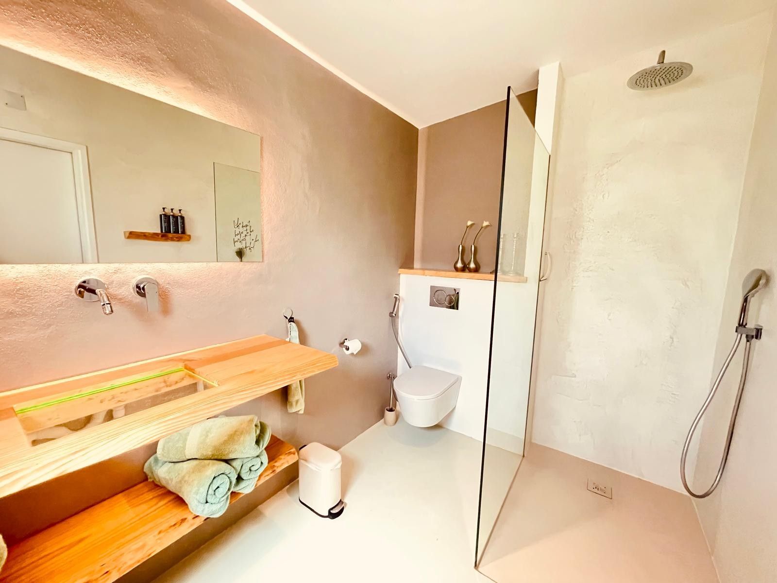 Un baño moderno con tocador de madera, cabina de ducha con mampara de vidrio y un inodoro blanco.