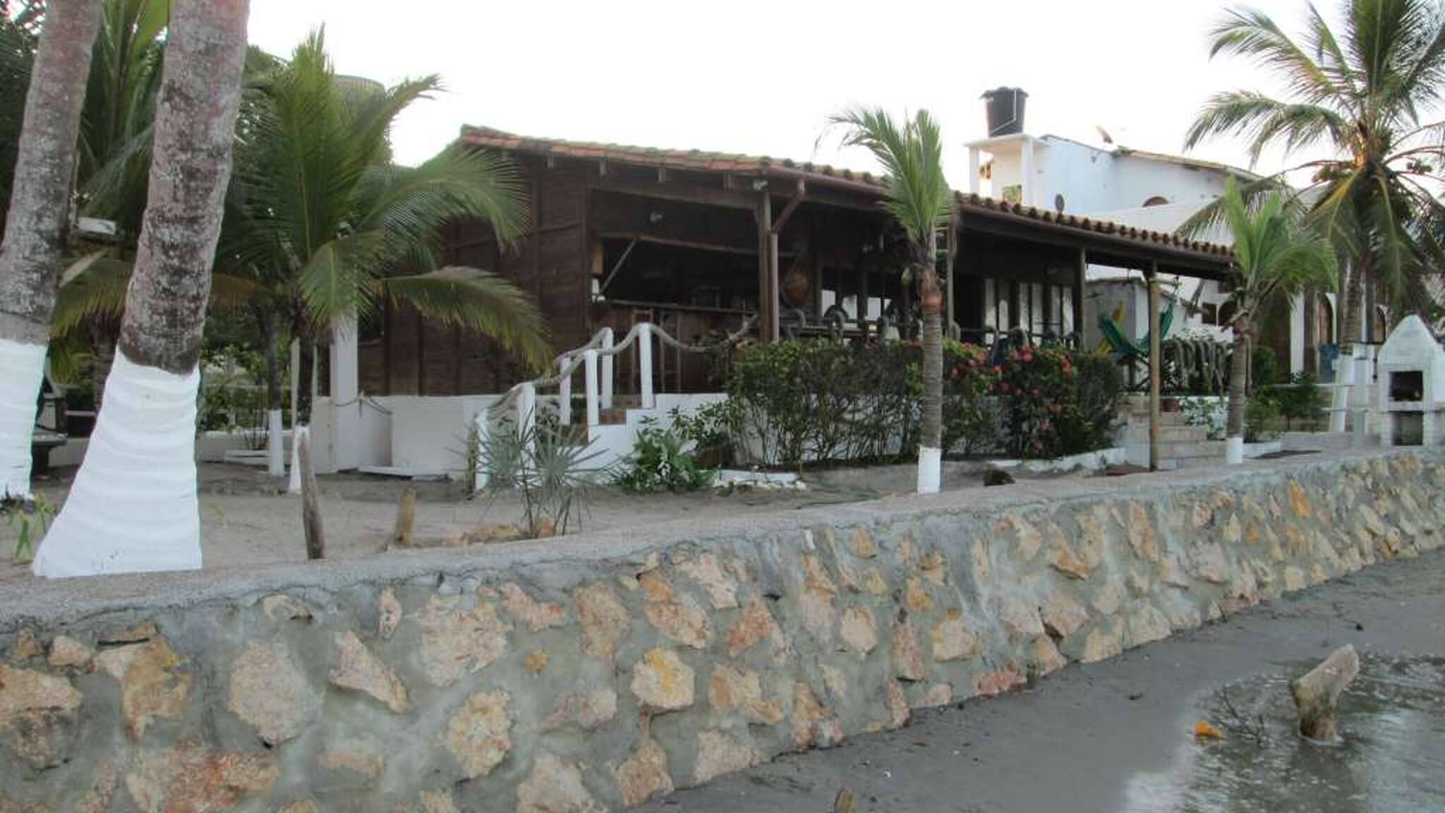 A coastal building with a stone wall, palm trees, and a small water feature.