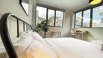 Una camera d'hotel con un letto, una scrivania, una sedia, una pianta e ampie finestre.