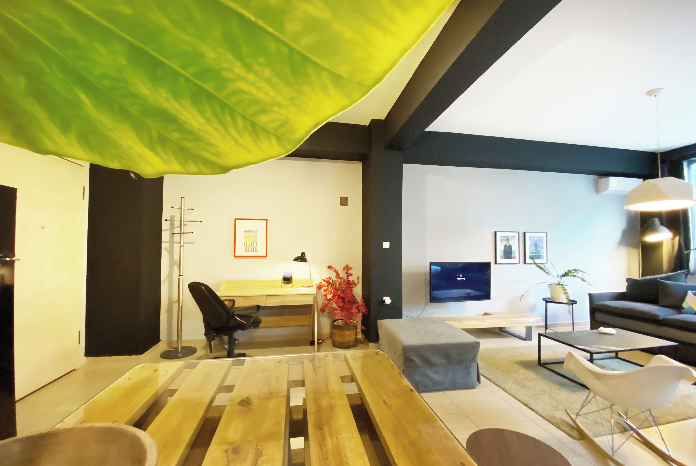 Un salon moderne avec un plancher en bois, un bureau avec une chaise, un canapé, un téléviseur et une grande fenêtre.