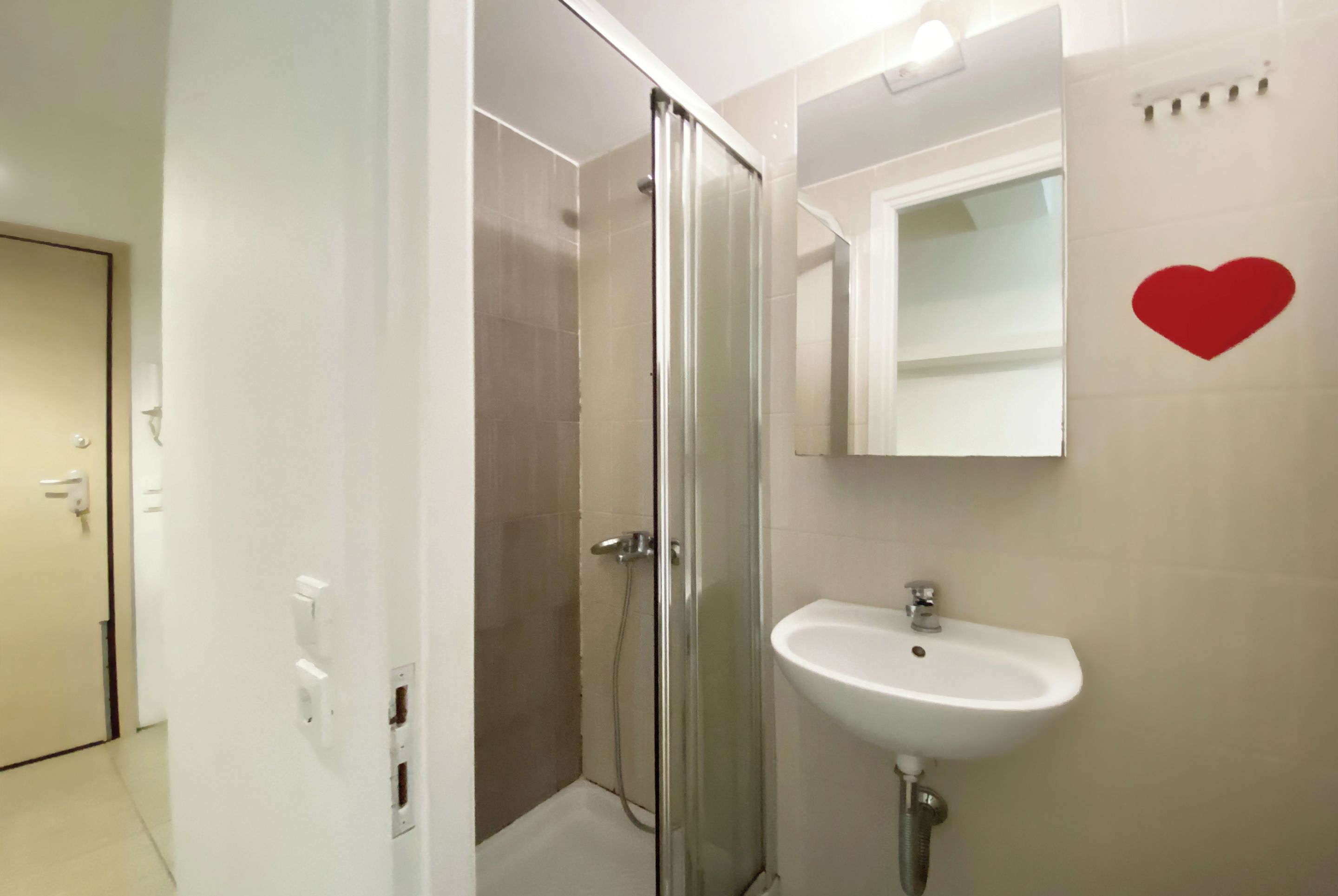 Une salle de bain avec une douche à parois de verre, un lavabo blanc et un miroir décoré d’un cœur rouge.