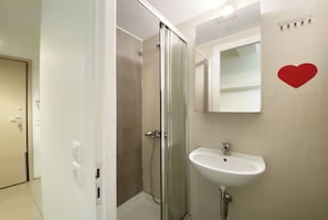 Een badkamer met een glazen douchecabine, een witte wastafel en een spiegel met een rode hartdecoratie.