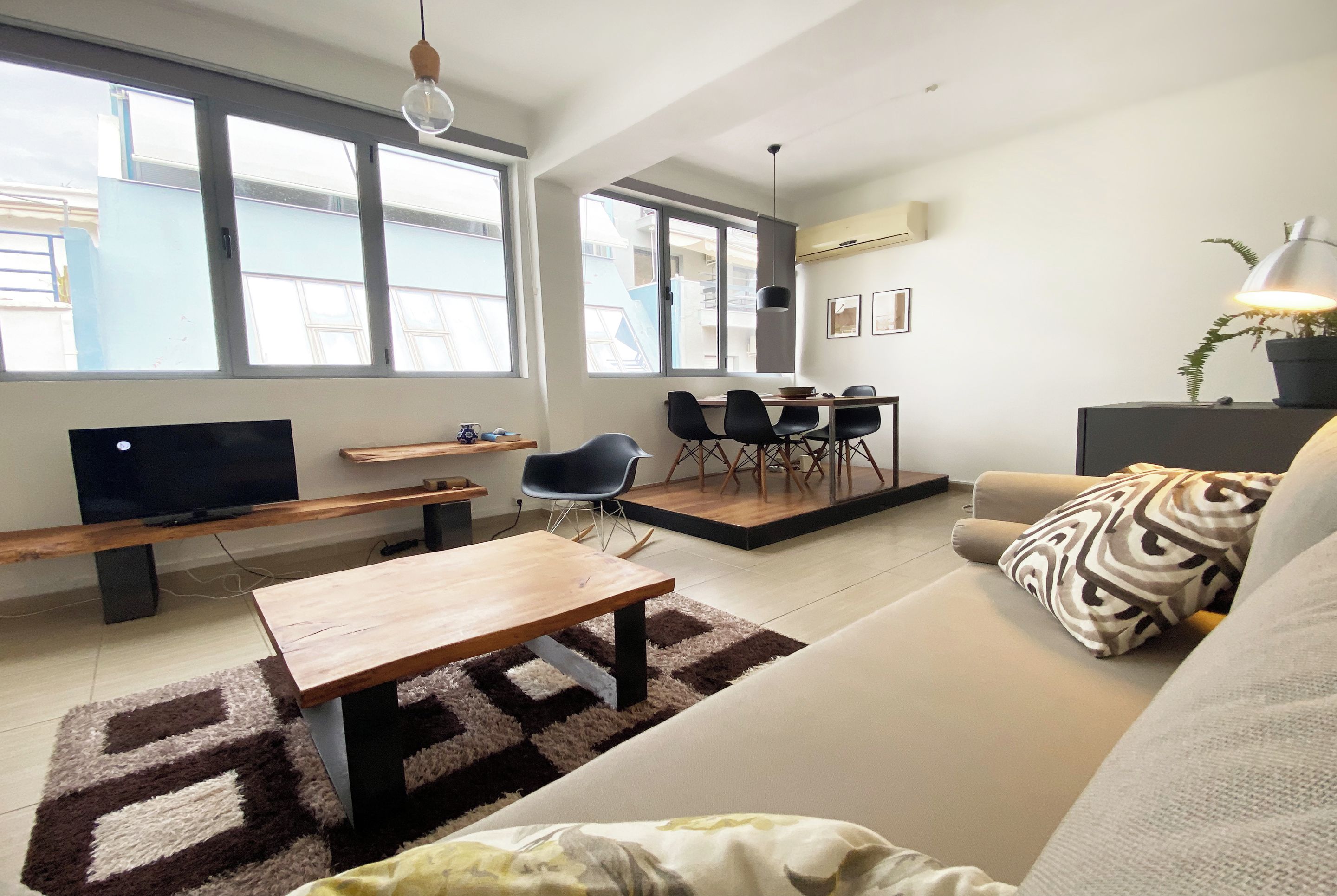 A modern living room with a sofa, a coffee table, a TV, and a dining area with chairs and a table.