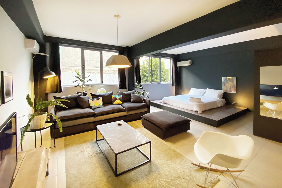 Een moderne woonkamer met een bank, salontafel en een bed met een witte matras.