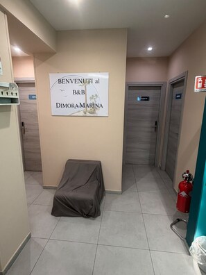 En hall med en skylt för B&B Dimora Marina, en brandsläckare och ett föremål som är täckt med något.