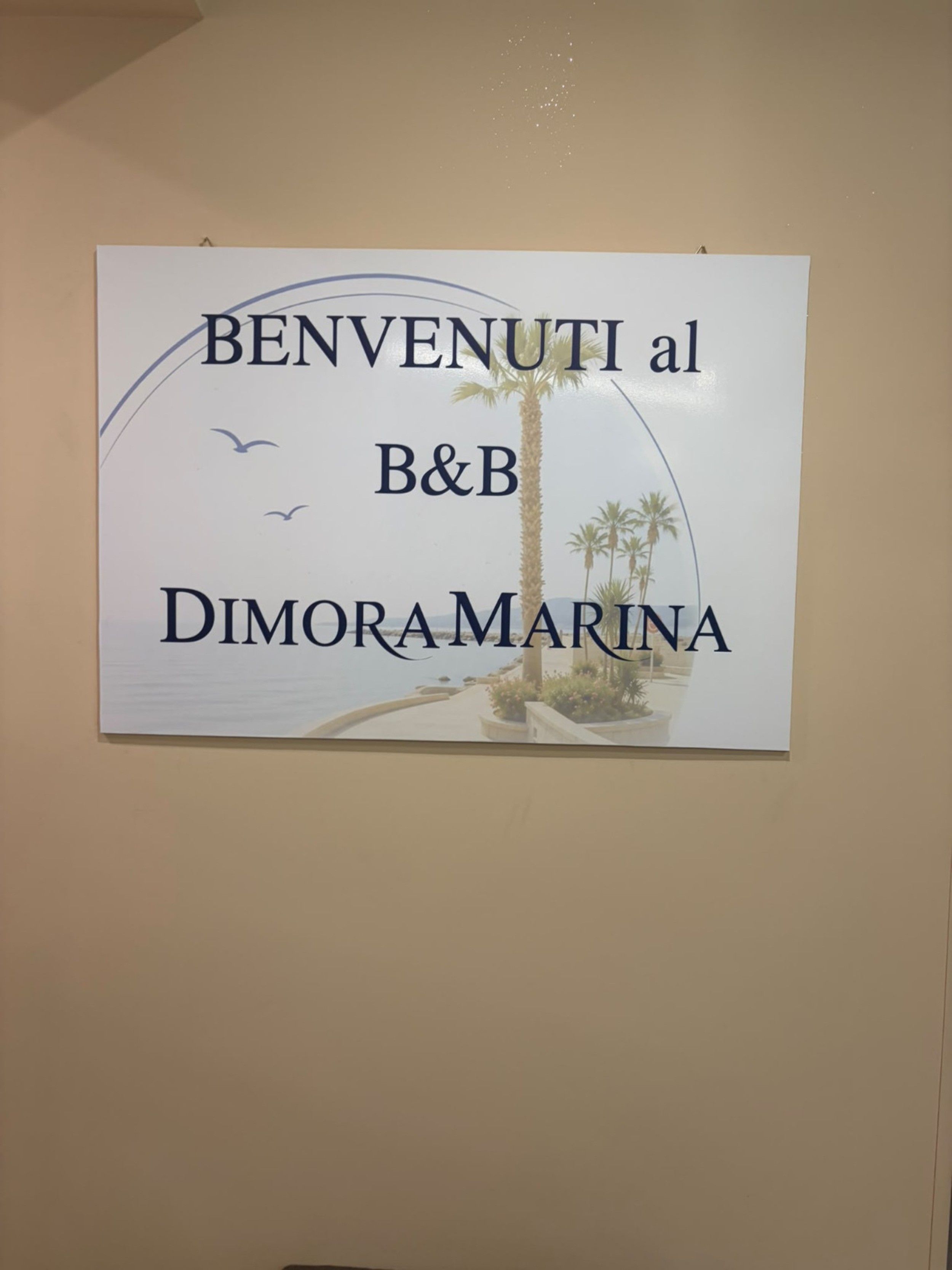 A welcome sign for B&B Dimoramara with a coastal landscape and palm trees.