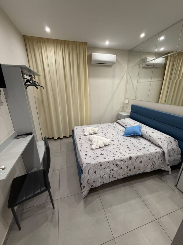Una camera d'albergo con un letto, una scrivania, una sedia e un condizionatore d'aria.