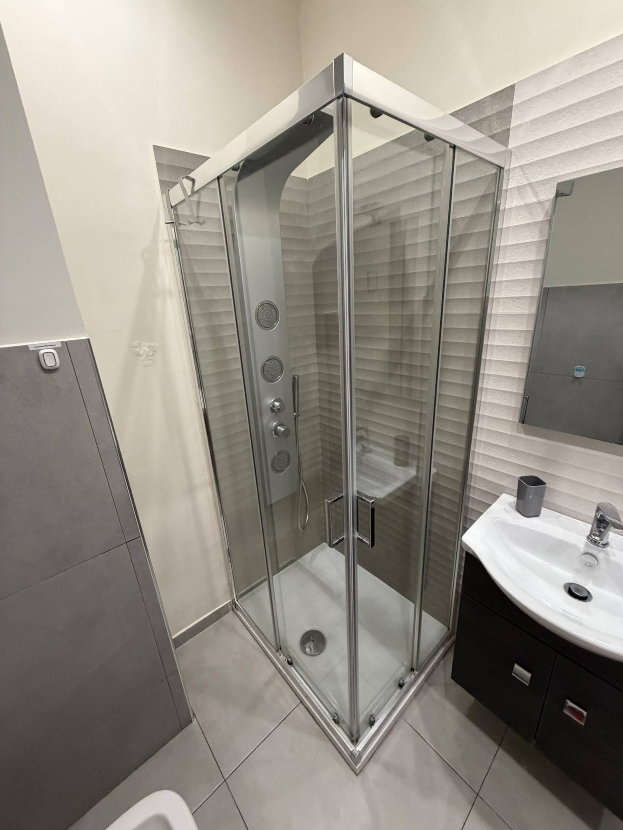 Ein modernes Badezimmer mit einer gläsernen Duschkabine, einem weißen Waschbecken und einem dunklen Schrank.