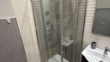 Ein modernes Badezimmer mit einer gläsernen Duschkabine, einem weißen Waschbecken und einem dunklen Schrank.