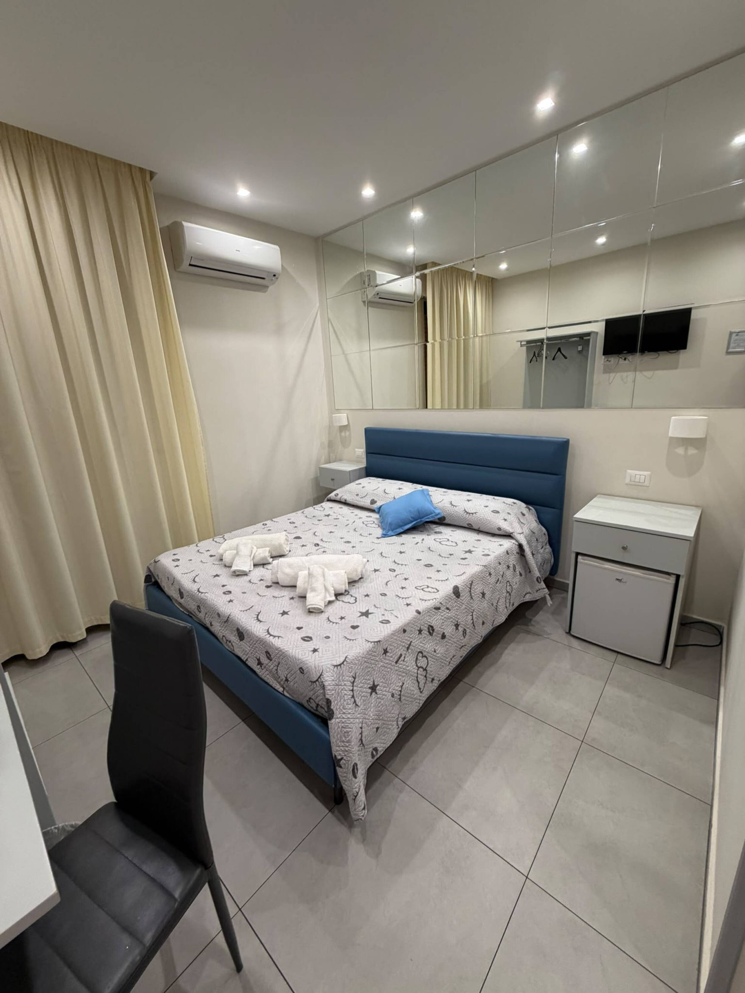 Une chambre à coucher moderne, équipée d’un lit, d’une chaise, d’une table de chevet et d’un petit réfrigérateur.