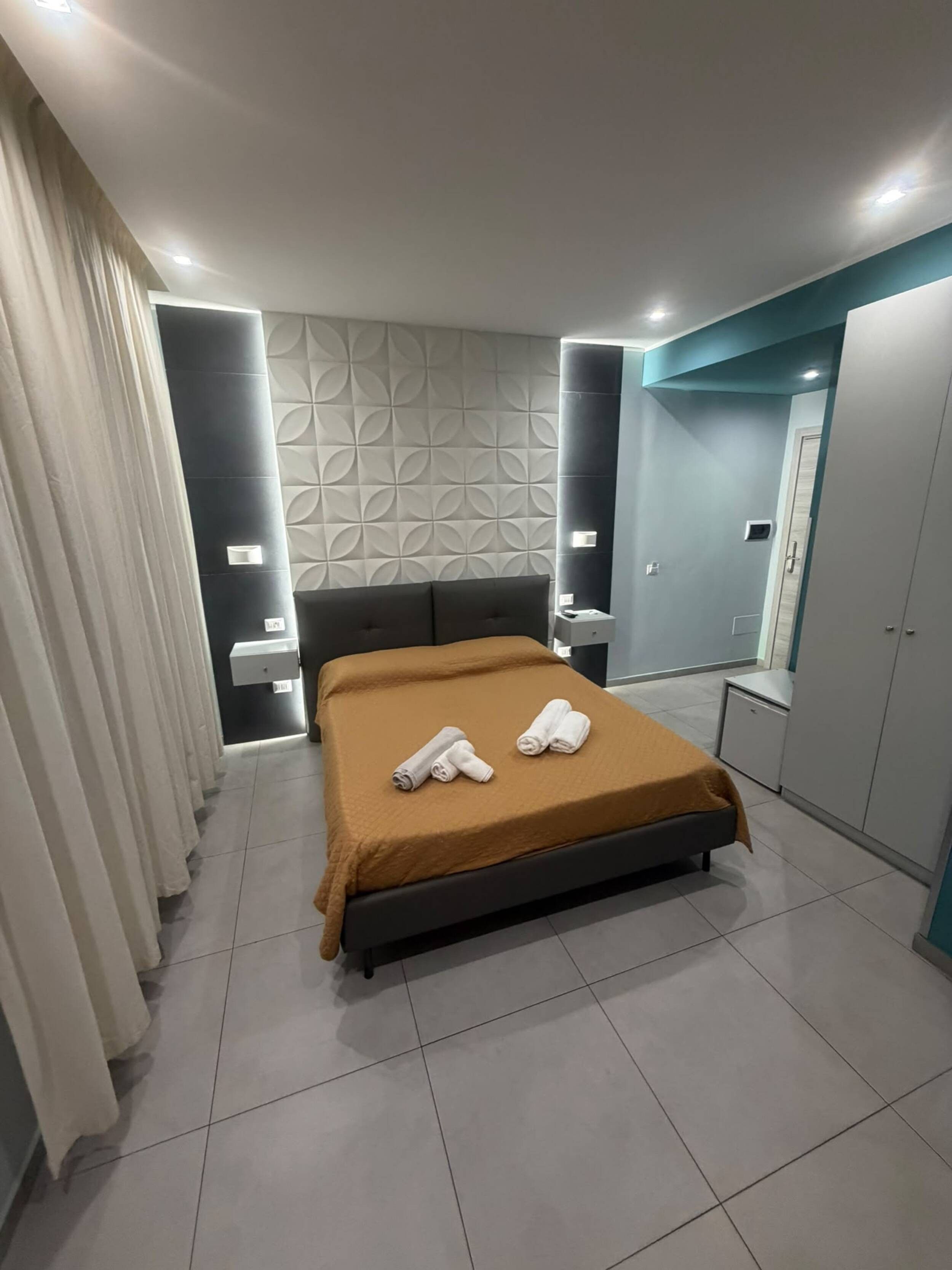 Un dormitorio moderno con cama, cortinas, cabecero, una pared con diseño geométrico y armario.