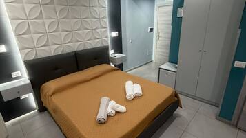 Une chambre à coucher moderne avec un lit, deux serviettes enroulées, une table de chevet, une armoire et une salle de bain visible au fond.