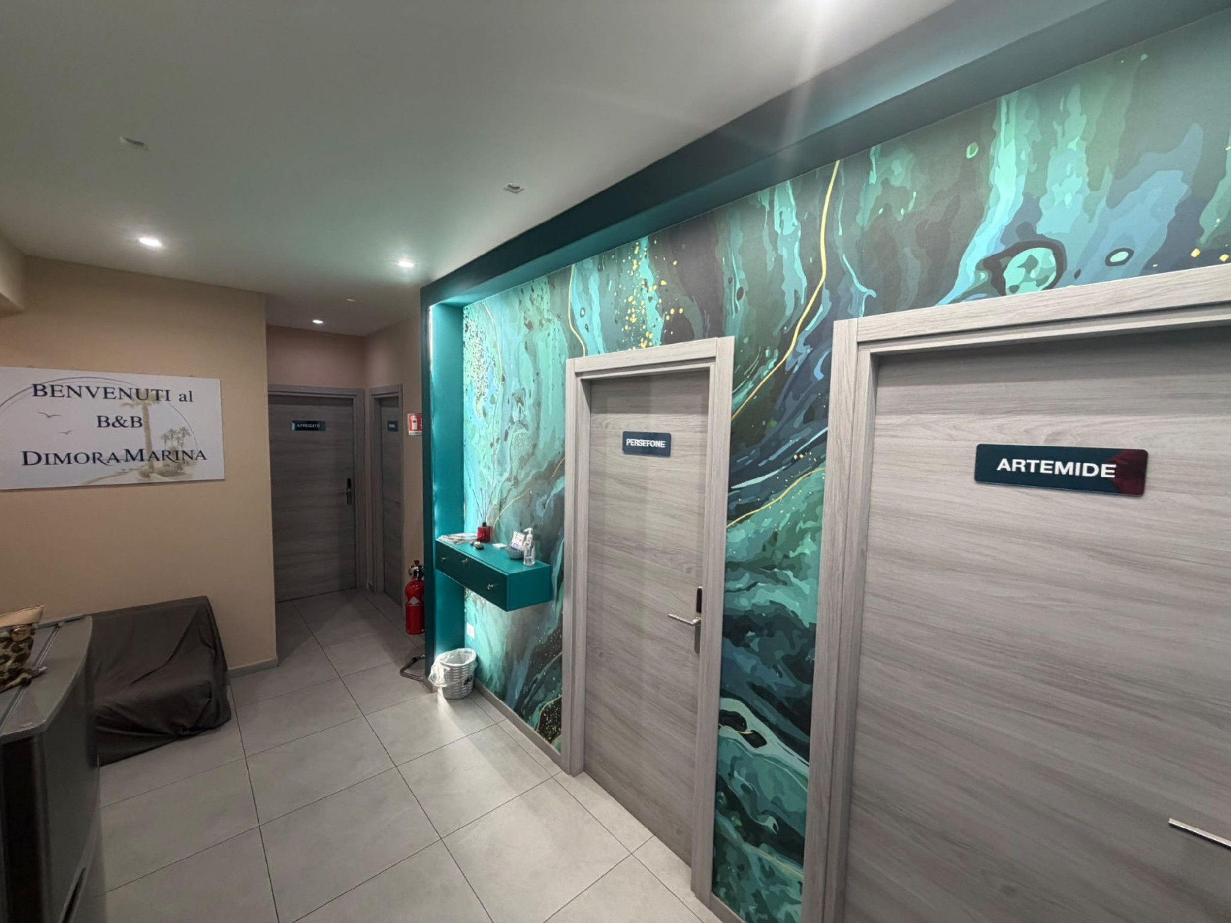A hallway with a marble wall mural, a reception desk, and two doors labeled 'PERSEFONE' and 'ARTEMIDE.'