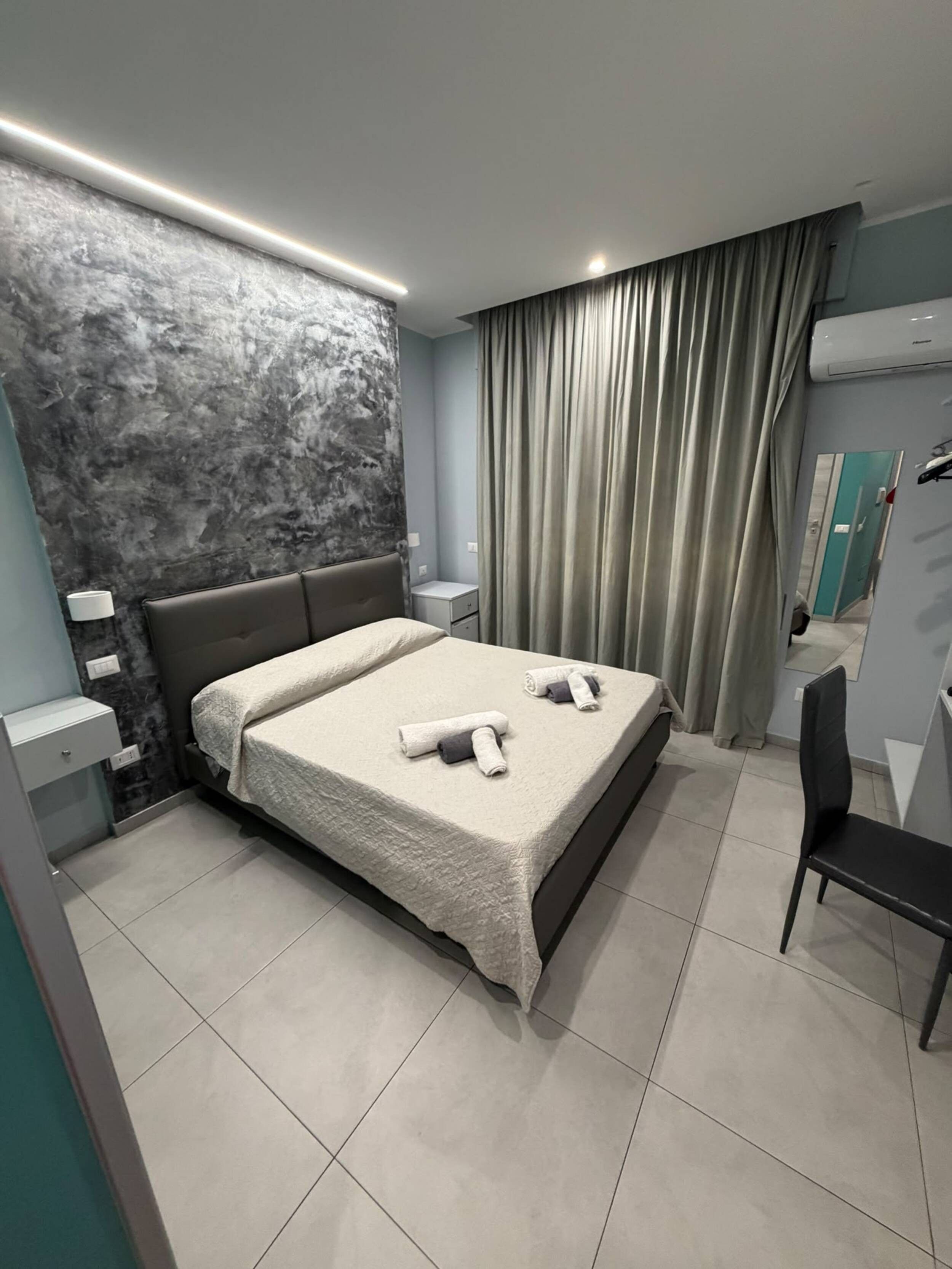 Ein modernes Hotelzimmer mit einem großen Bett, einem Nachttisch, einem Sessel und einer Wand-Klimaanlage.