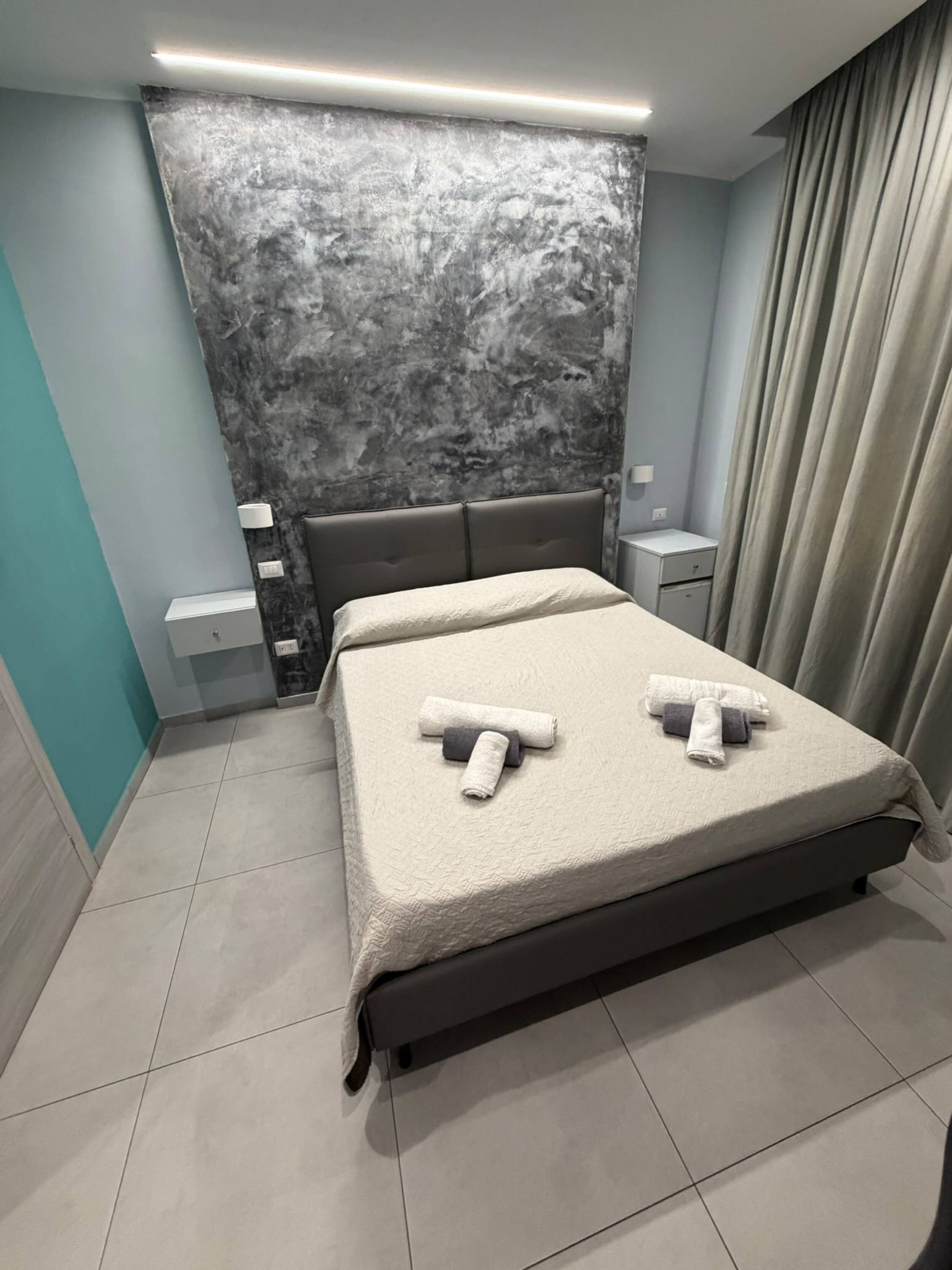 A hotel room with a bed, a nightstand, a lamp, and a curtain.
