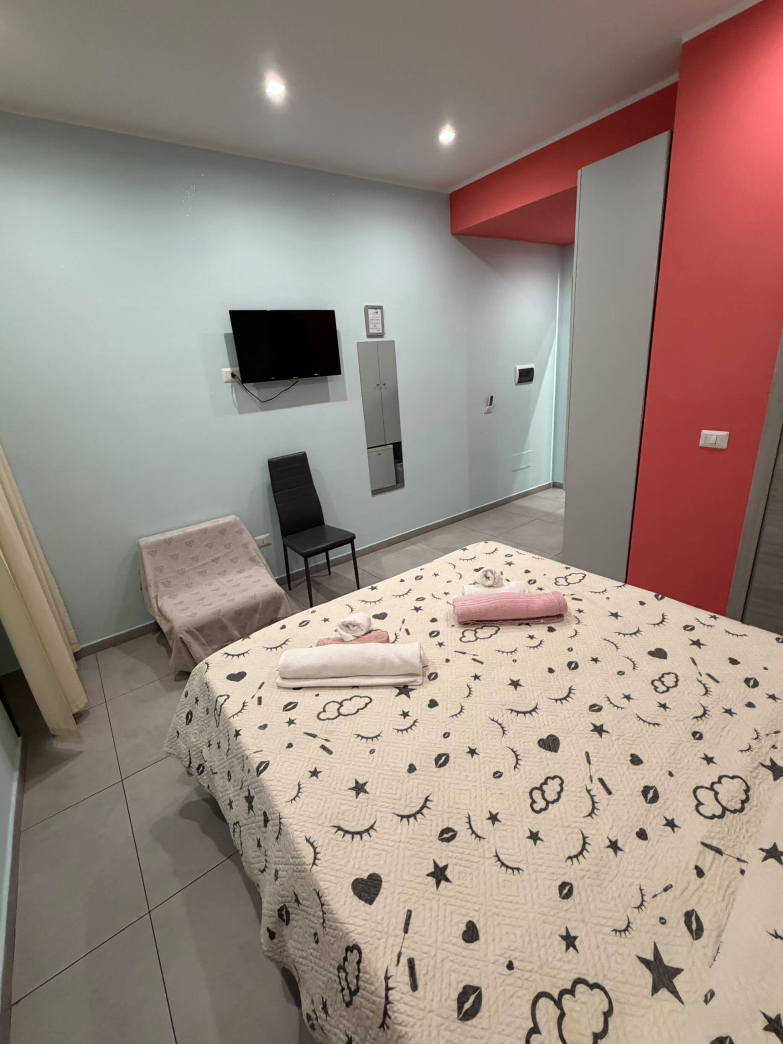 A bedroom with a bed, a chair, a TV, and a wardrobe.