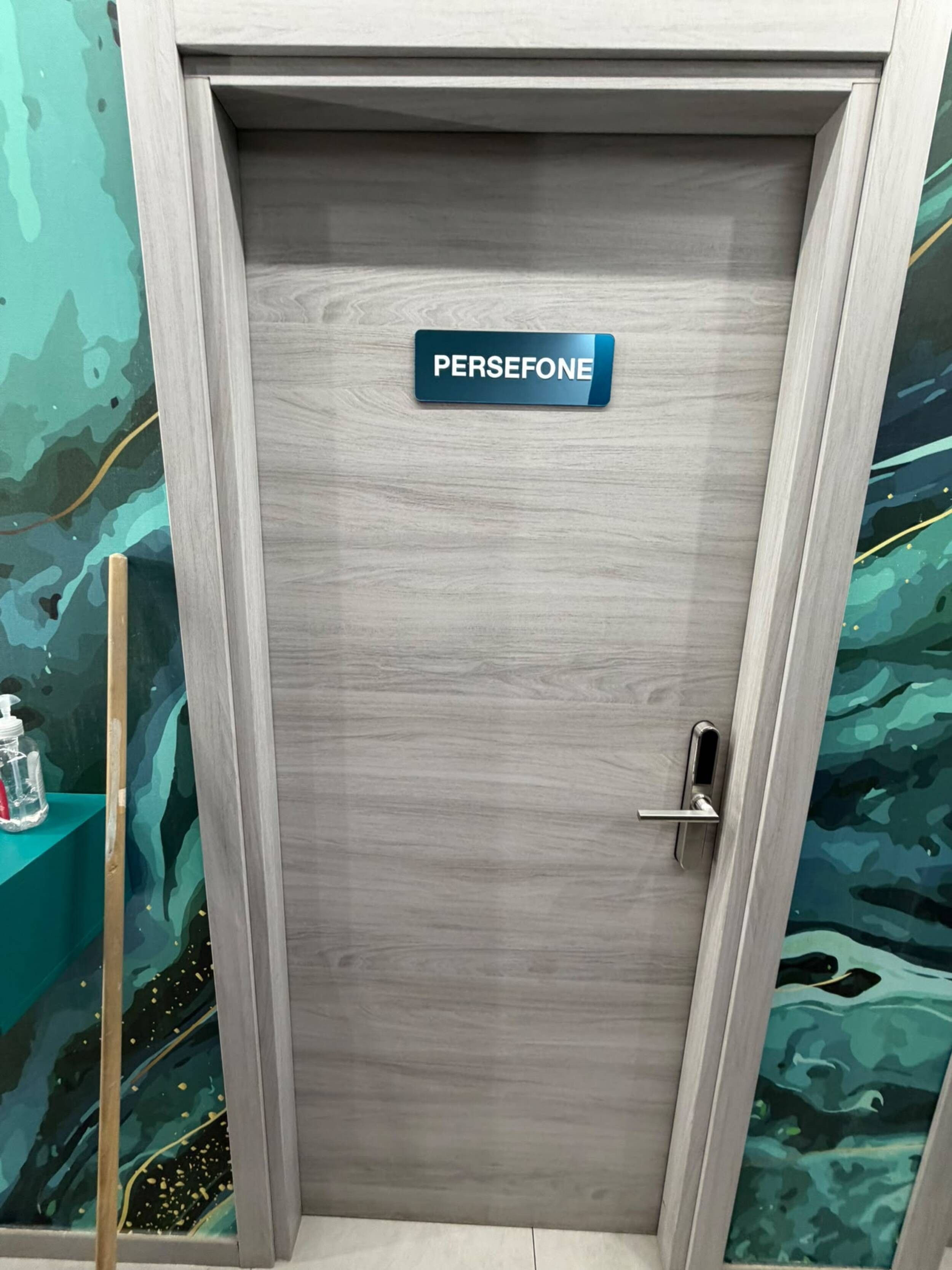Een deur met een bord waarop 'PERSEFONE' staat en een metalen handgreep.