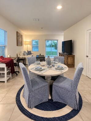 A dining area with a round table set for four, surrounded by striped chairs, a TV on the wall, and a view through a sliding door. - Charming 3-bedroom townhome  Close 2 Beaches in marvelous St. Augustine (St. Augustine)