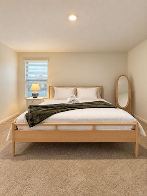 Quarto com cama, mesa de cabeceira, luminária, espelho e janela com persianas.