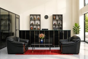 Un espace d’accueil avec un comptoir de réception noir, deux canapés en cuir noir, un tapis rouge et un vase rempli de fleurs.