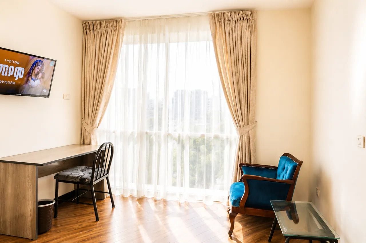 A room with a desk, two chairs, a television, and a window with curtains.