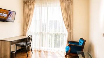 A room with a desk, two chairs, a television, and a window with curtains.