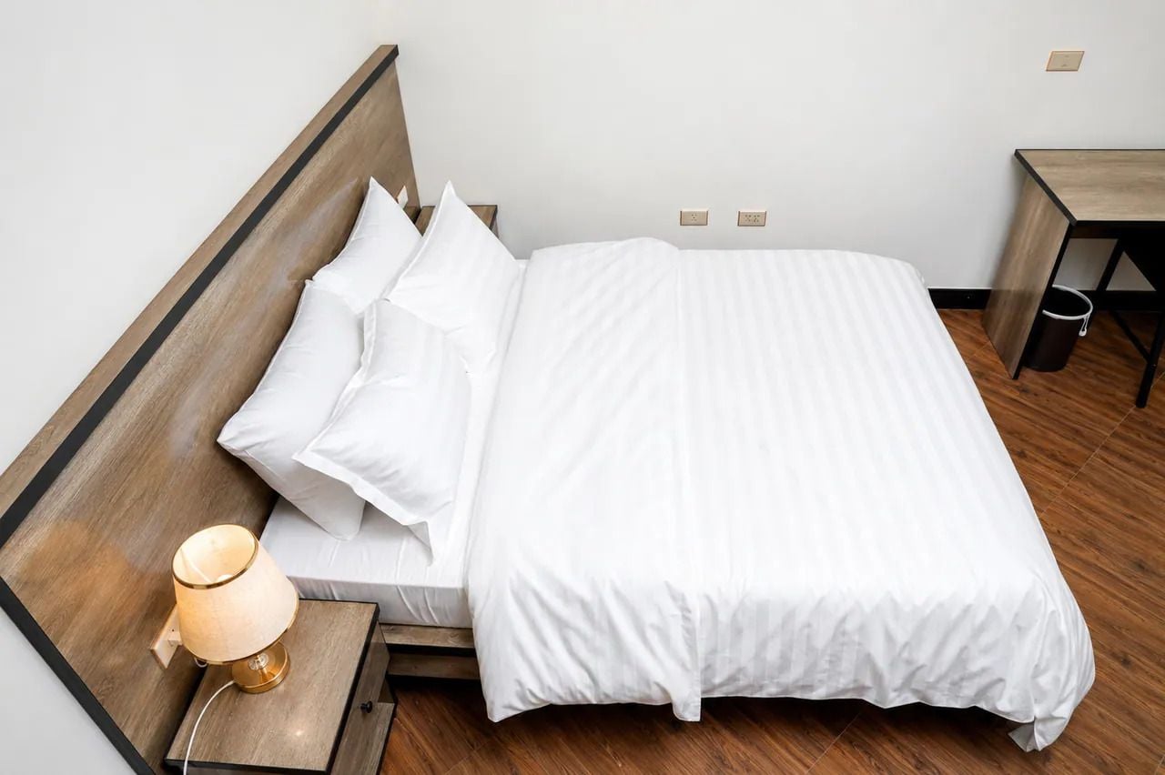 A neatly made bed with white linens and pillows, a bedside lamp, and a wooden nightstand.