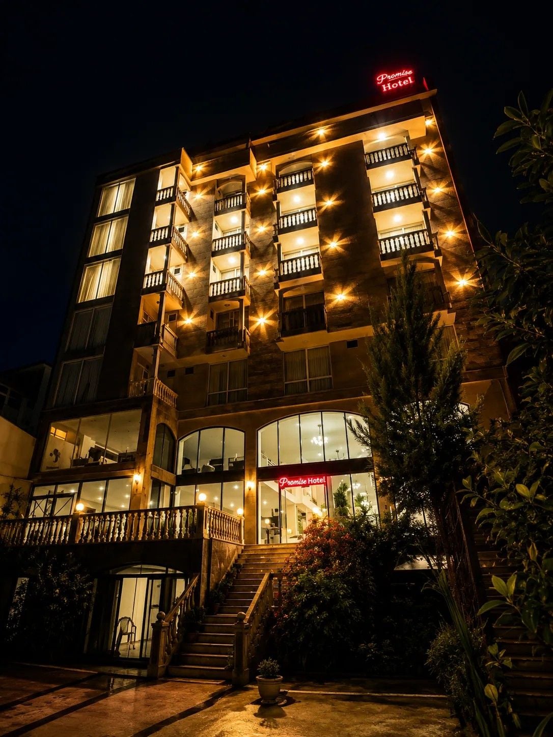 Hotel de diverses plantes amb un destacat rètol de 'Promise Hotel', una escala central i façana de vidre.