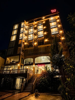 Un hôtel à plusieurs étages, reconnaissable à son grand panneau « Promise Hotel », à son escalier central et à sa façade en verre.