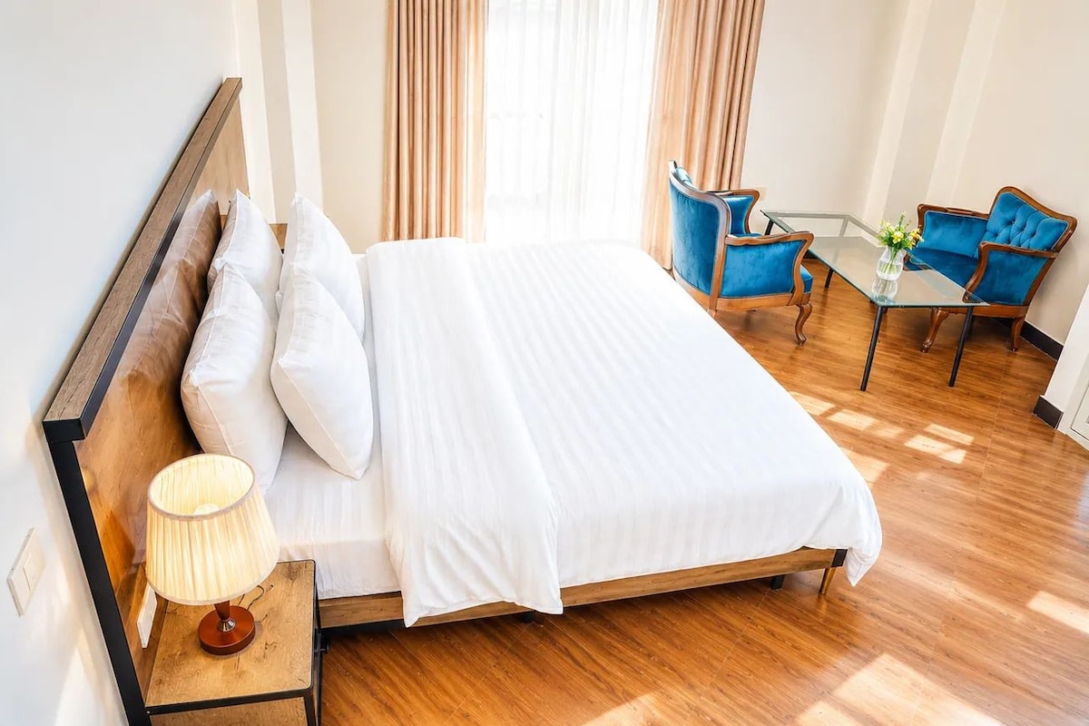 Une chambre d’hôtel comprenant un lit, une table de chevet, une lampe, une table avec des chaises et une vue sur l’extérieur.
