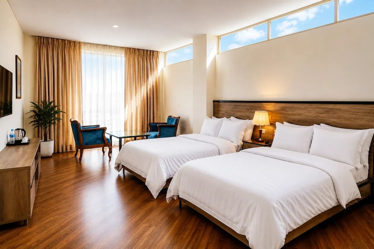 Une chambre d’hôtel avec deux lits, un bureau, une chaise, une lampe et une fenêtre avec des rideaux.