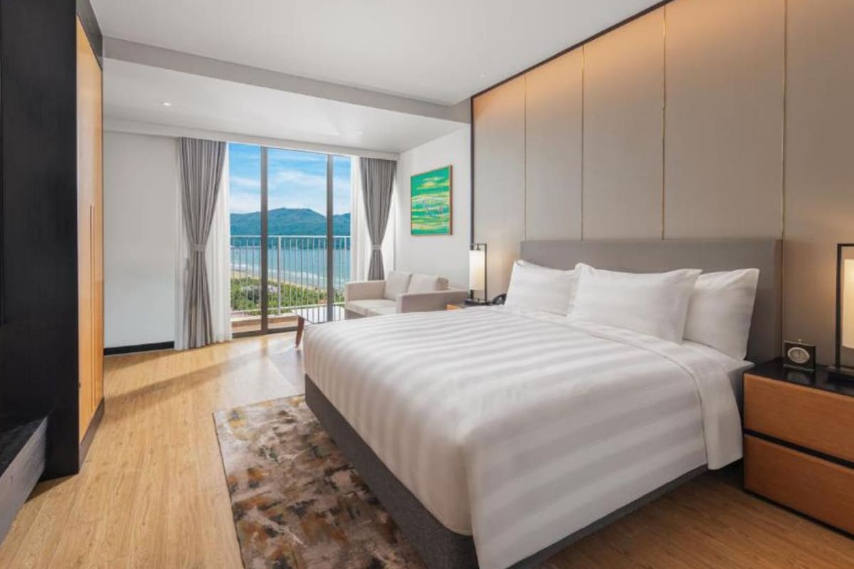 Una habitación de hotel moderna con una cama grande, un escritorio, una silla y vistas al exterior.
