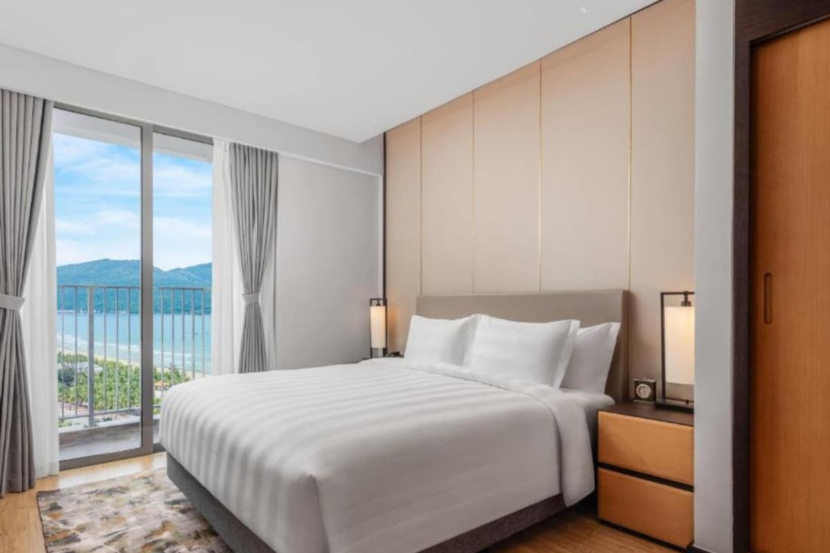 Habitación de hotel con una cama grande, una mesita de noche, un armario de madera y vistas al exterior.