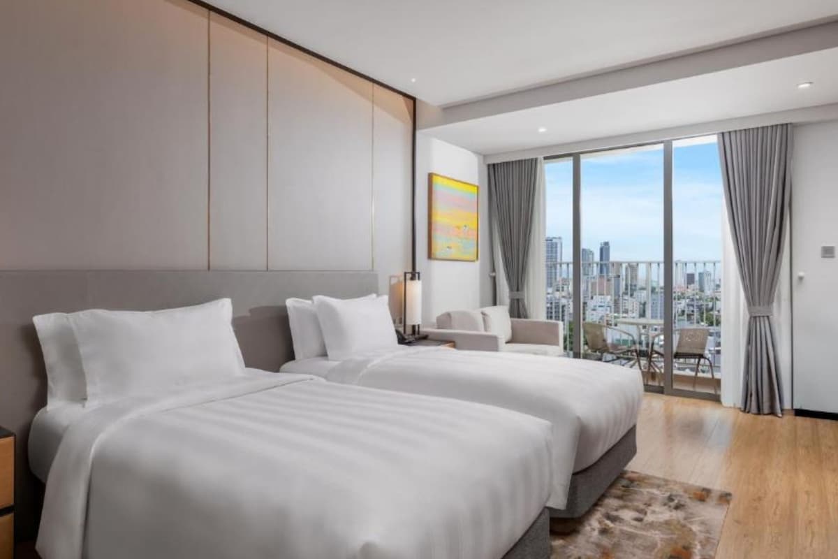 Una habitación de hotel moderna con dos camas grandes, vistas a la ciudad y un balcón.