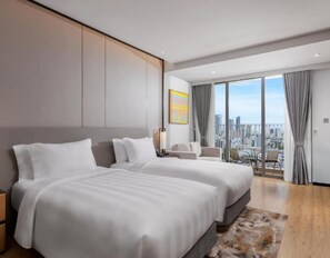 Una habitación de hotel moderna con dos camas grandes, vistas a la ciudad y un balcón.