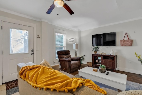 A living room with a sofa, a recliner, a coffee table, a TV, and a ceiling fan.