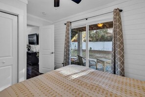 A bedroom with a bed, a sliding glass door leading to an outdoor area, and a television in the corner.