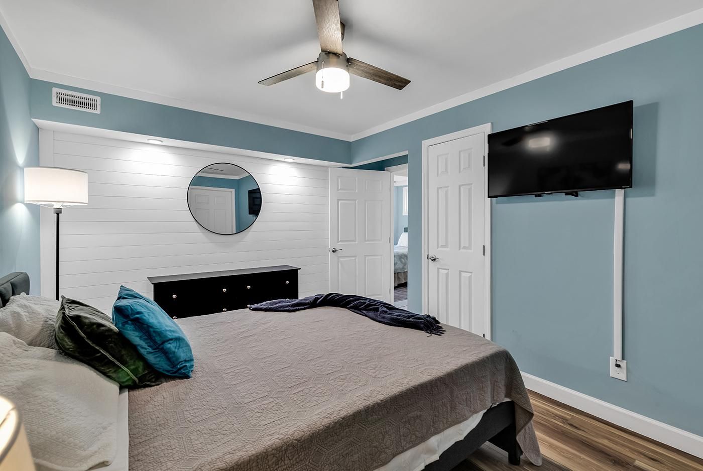 A bedroom with a bed, a ceiling fan, a TV, and a door leading to another room.