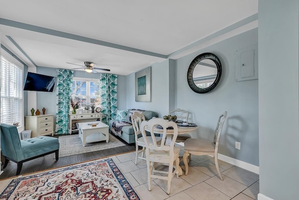 A living room with a television, sofa, coffee table, and a dining area with chairs and a table.